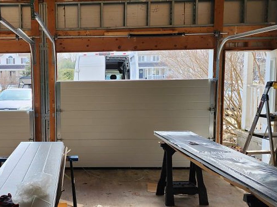 Installation part way through, with a new insulated door section in the opening and the remaining sections laid out on trestles behind it