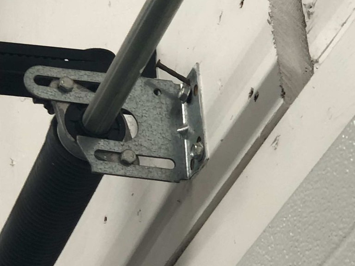 Centre bearing plate bolted to the header above a garage door, carrying the torsion shaft, with the stationary cone and spring end fitting alongside