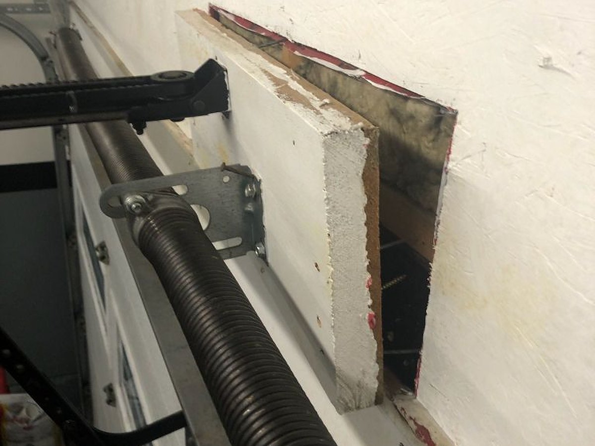 Header wall opened up next to a torsion spring so the structural backing behind the anchor bracket can be seen and tested